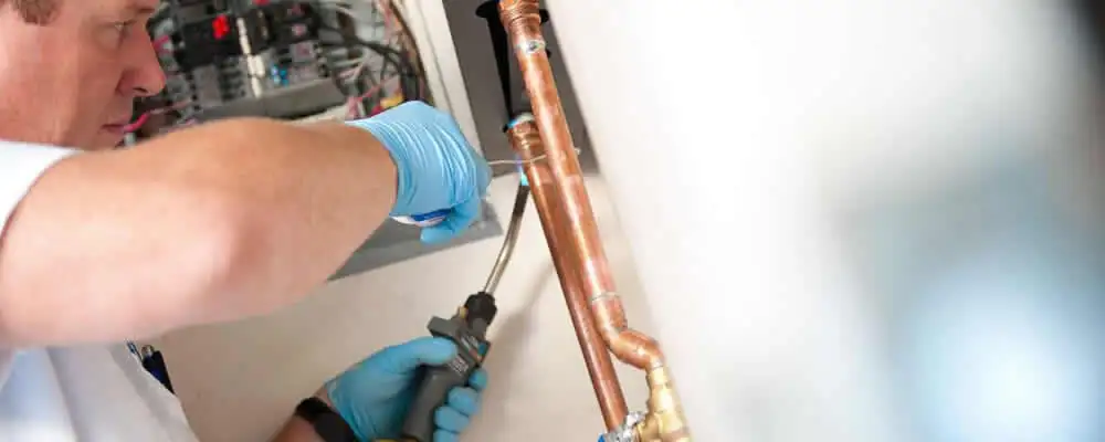 Water heater repair technician testing copper pipe connections and controls in Virginia Beach, VA
